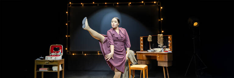 Nainen tanssii jalka ylhäällä näyttämöllä.